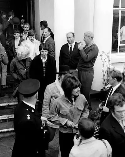 A policeman and a crowd of onlookers outside the hotel's front porch as members of the Beatles come down the steps
