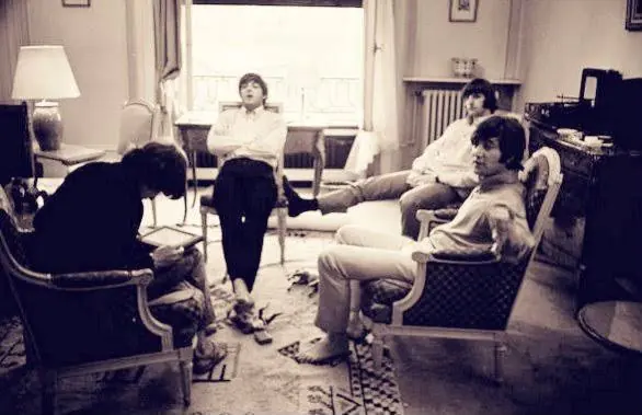 The Beatles relaxing in armchairs in Room 20 at the hotel in 1965, one of them barefoot