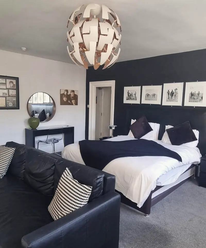 The Beatles Suite: a double bed with black and white bedding against a black wall, under a row of framed black and white photographs of the band, with a black leather sofa in front