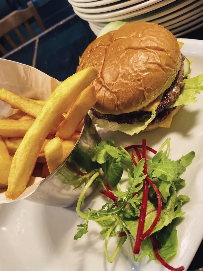 A burger in a glazed bun with chips and salad