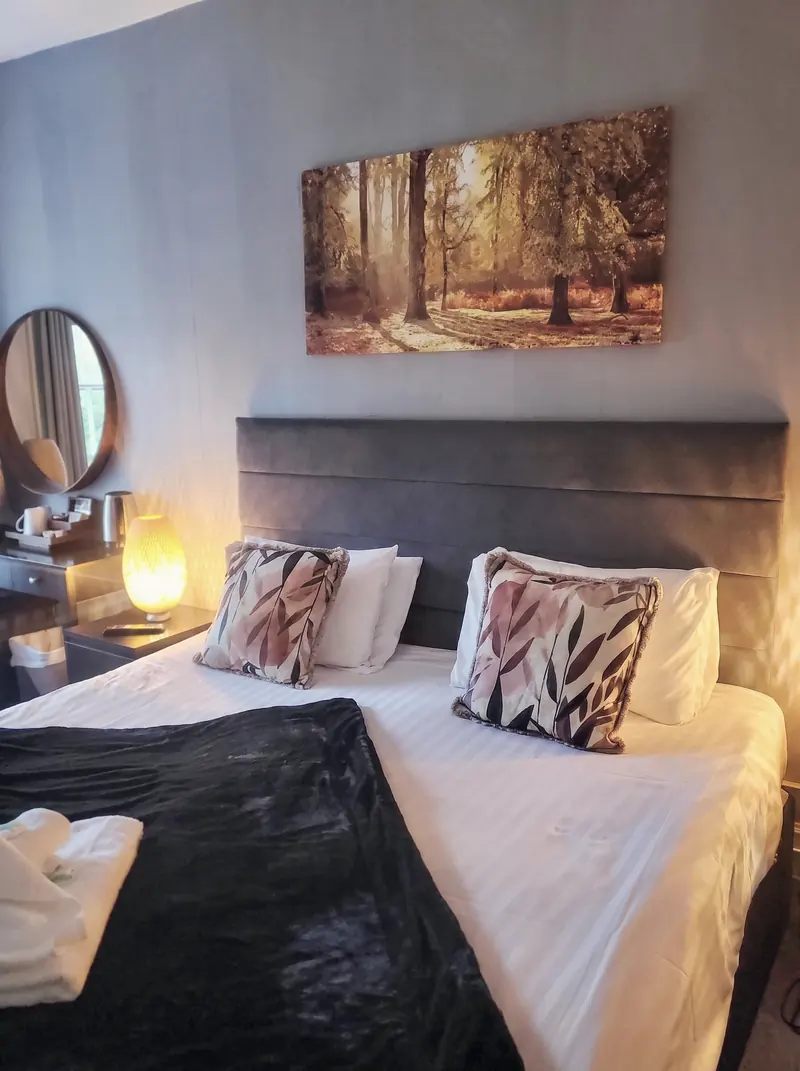 A double room with a grey upholstered headboard and a woodland print above the bed