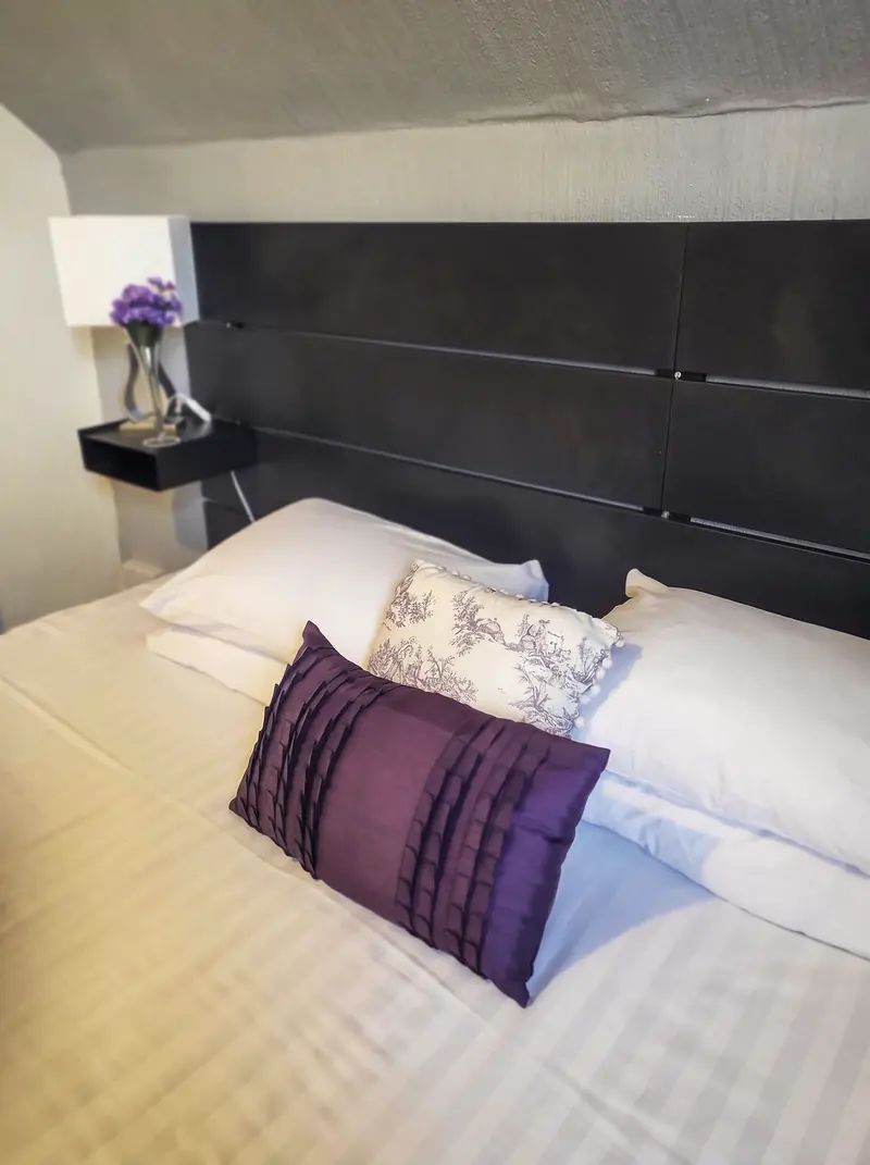 A double bed with white linen and a purple cushion