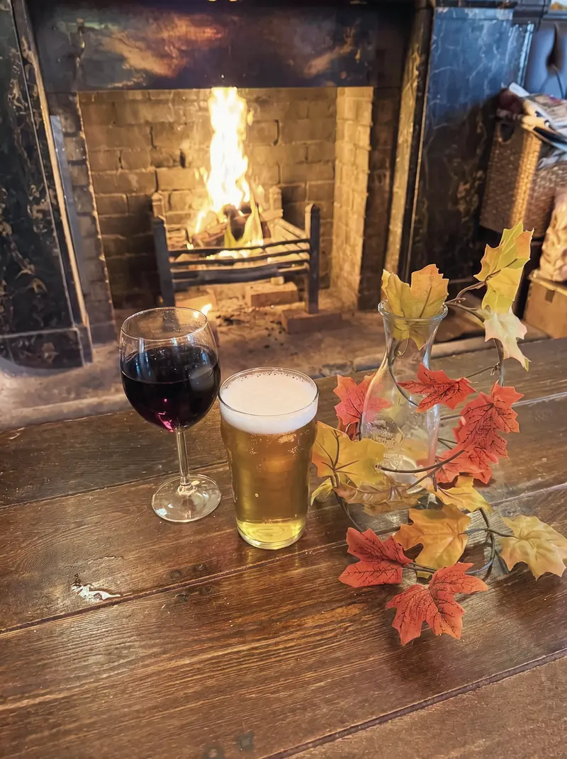 A glass of red wine and a glass of beer on a table in front of the fire