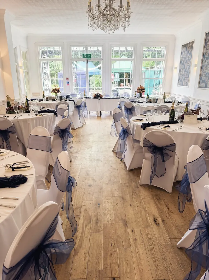 Function room set with round tables, white chair covers and navy sashes, with windows onto the garden