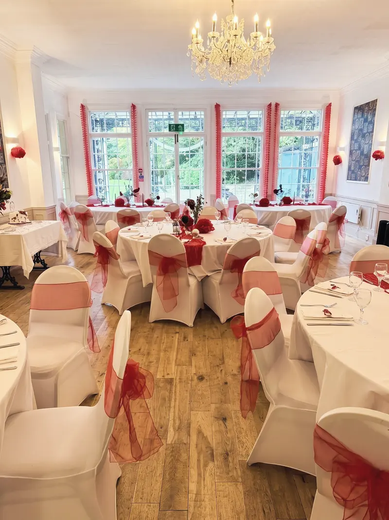 Function room dressed with white chair covers and red sashes under a chandelier