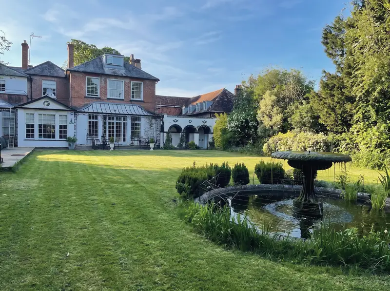 The back of The Antrobus Hotel seen across the lawn, with the stone fountain and pond in the walled garden