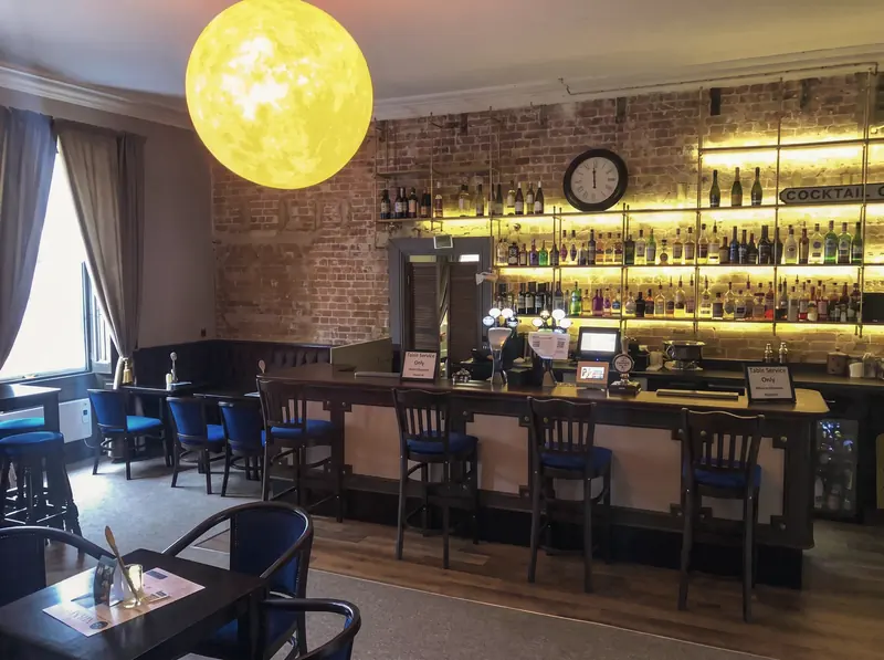 The lounge bar counter with backlit shelves of spirits against an exposed brick wall