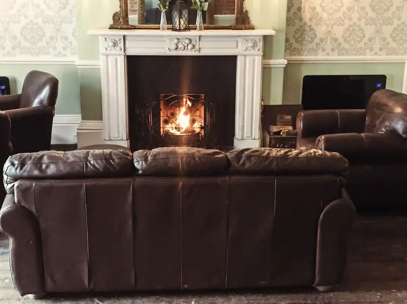 A leather sofa in front of a lit fire in a white fireplace