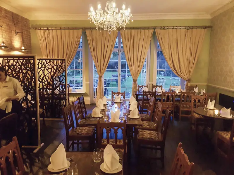 The restaurant laid for dinner, with dark wood chairs, a chandelier and tall draped windows