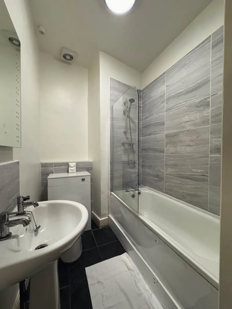 The en-suite bathroom of the Small Double Room: a basin, a WC and a bath with a shower and glass screen, in grey marble-effect tiles