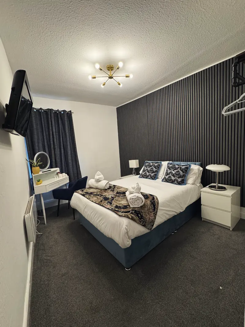 The Small Double Room from the door: the double bed between white bedside tables and lamps, with a dressing table, round mirror and navy velvet chair by the window
