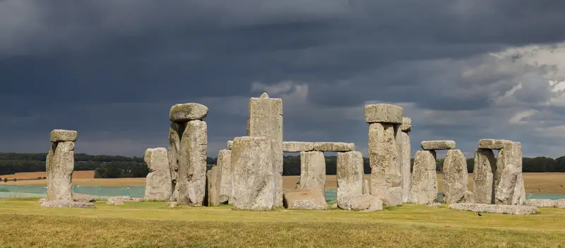 Stonehenge seen across the grass under a dark, stormy sky